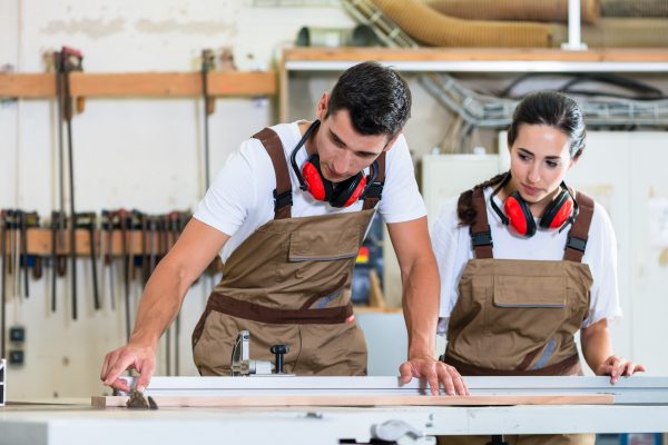 Carpenter And Apprentice Working Together In Workshop